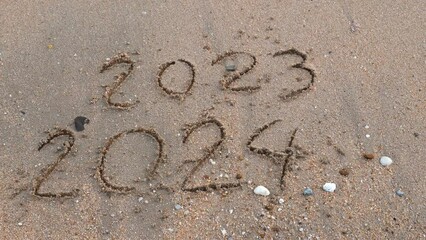Wall Mural - message year 2023 replaced by 2024 written on beach sand background. goodbye 2023 - 2024 lapping wav