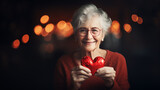 Fototapeta  - A happy elderly woman holds a red heart in her hands.