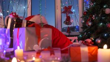 Santa Claus At Christmas Party Takes Out Of Beautiful Colorful Holiday Gifts, Placing Them On Table Among Burning Candles Next To Christmas Tree Decorated With Balls, Garlands And Shiny Tinsel.