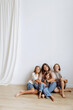 © Kaplitskaya Love - Happy smiling mother and three daughters in casual and denim clothes sit hugging on a wooden floor on a white background. The concept of family, motherhood and successful life.