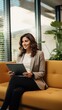 © ArtCookStudio - A woman using a tablet device, smiling and sitting on a couch in a modern office space