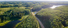 An Aerial View Of An Extensive Boreal Forest With Mixed Tree Types And Scattered Small Lakes. A Gravel Road Winds Through The Forest. The Sun Is Reflecting Off One Of The Lakes Creating A Sun Glare On