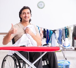 Wall Mural - Young man in wheel-chair doing ironing at home