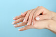 Woman with white polish on nails against light blue background, closeup
