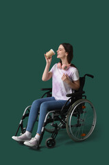 Wall Mural - Young woman in wheelchair with cup of coffee on green background