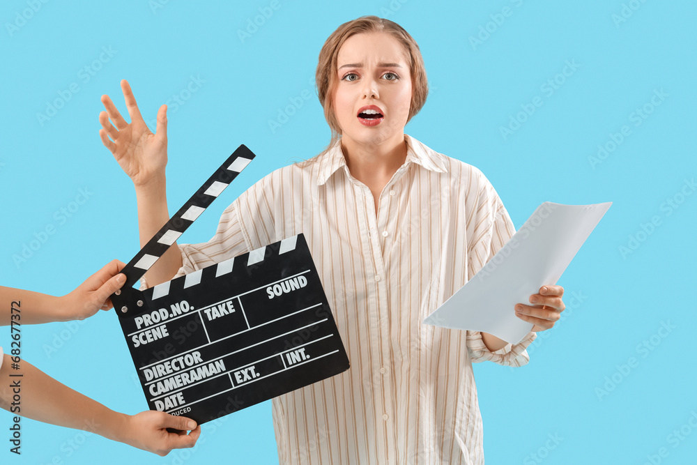 Beautiful actress with film script and movie clapper on blue background