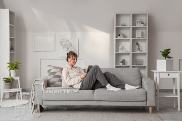 Wall Mural - Young woman with tablet computer relaxing on sofa at home