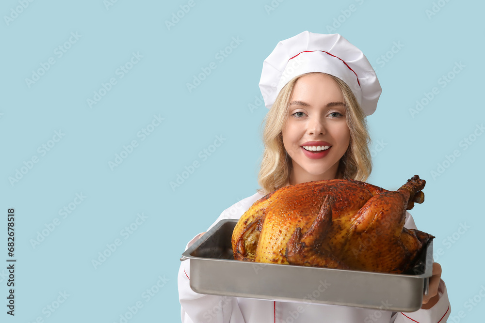 Young female chef with tasty baked turkey on blue background. Thanksgiving Day celebration