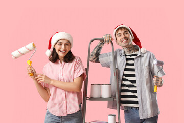 Sticker - Young couple in Santa hats with painting tools on pink background