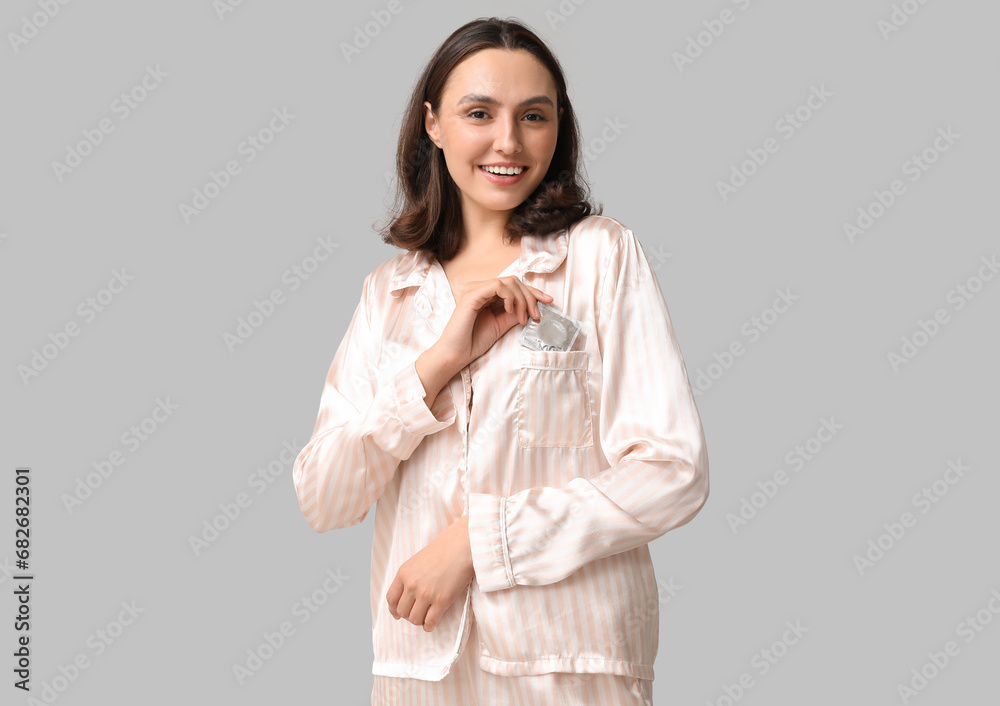 Beautiful young woman putting condom on grey background. Safe sex concept