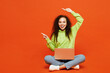© ViDi Studio - Full body happy young IT woman of African American ethnicity she wear green hoody casual clothes sit hold use work on laptop pc computer point aside on area isolated on plain red orange background.
