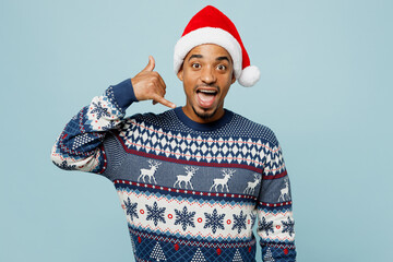 Wall Mural - Young excited man wear knitted sweater Santa hat posing doing phone gesture like says call me back isolated on plain pastel blue background. Happy New Year 2024 celebration Christmas holiday concept.