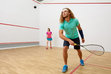 Squash male player with racket playing game with female friend