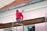 Fototapeta  - Worker on scaffolding paint facade wall of historic building. Utility worker paints building facade. Repair and restoration building facade. Man painting house wall with paintbrush