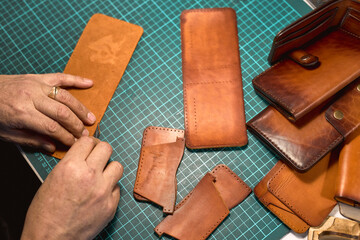 Wall Mural - process of making a leather wallet. close up cropped photo. top view. small business. lifestyle. hobby. leather crafting, artisan cuts out patten. old man burnishes the two short edges