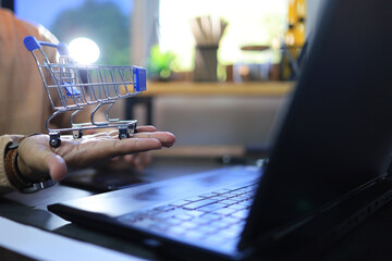 Wall Mural - Businessman holding shopping cart in front of laptop screen represent to on line store or e commerce marketing connection