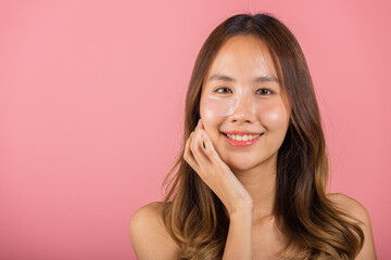 Anti aging. Asian beautiful young woman smiling mask cosmetic patches gel under the eyes, Portrait female applying medical hydrogel eye patch on face, studio shot isolated on pink background, skincare