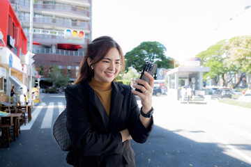 Smiling Asian businesswoman wearing a suit stands tall in the city using an application on her mobile phone. Read news on your smartphone fast connection Check outdoor mobile apps