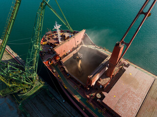 Aerial view of big cargo ship bulk carrier is loaded with grain of wheat in port at sunset