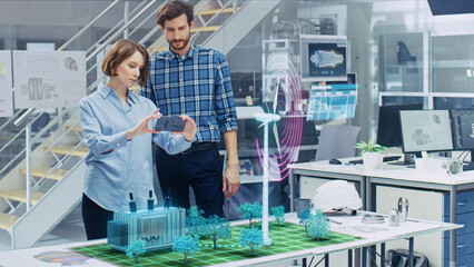 Wall Mural - green energy concept: two eco-engineers use augmented reality smartphone to design 3d wind turbine p