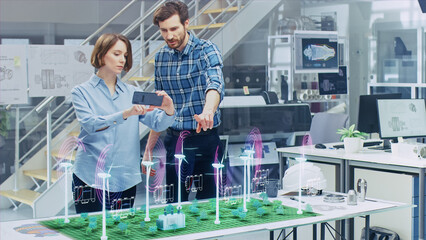 Wall Mural - green energy concept: two ecological engineers use augmented reality smartphone to design 3d wind tu