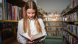 © 24K-Production - Cheerful, playful cute schoolgirl, going between bookshelves in the school library and choosing an inspiring book for reading
