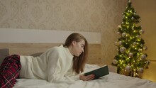 people, bedtime and rest concept - woman in pajamas reading book sitting in bed at night christmas concept