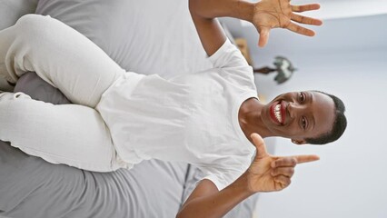 Sticker - Cheerful african american woman at home in her comfy bedroom, lying on bed, showing a joyful number seven sign with her fingers as she smiles away