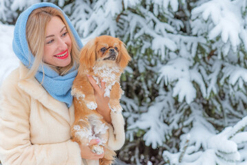 Smiling happy Lady with a young Pekingese cute dog in the snow park playing outdoor .Winter Christmas time. Doggo in good mood on a walk with his owner