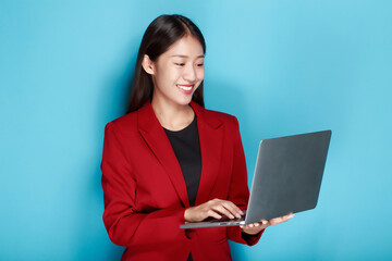 Poster - Portrait of a happy asian businesswoman working on laptop computer isolated over blue background
