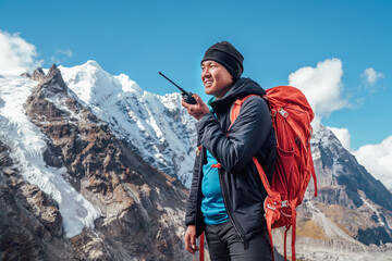 Wall Mural - portrait of sherpa man with backpack using walkie-talkie for calling rescue helicopter with mera pea