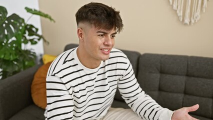 Sticker - Smiling young hispanic man relishes a fun conversation while comfortably seated on a sofa at home, emanating joy, confidence, and an attractive, relaxing aura