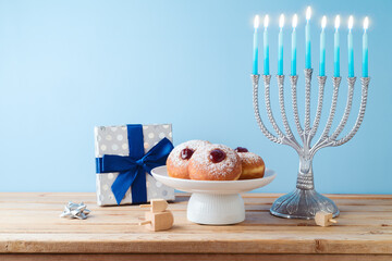 Wall Mural - Jewish holiday Hanukkah concept with menorah, traditional donuts and gift box on wooden table.