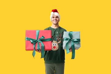 Canvas Print - Handsome young man in Santa hat holding Christmas gifts on yellow background