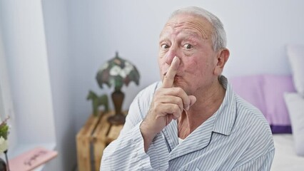 Poster - Shh! in the quiet bedroom, a confident senior man sits on the bed, wearing pyjamas. with a finger to his lips, he gestures for silence, a secret hinted in his calm expression.