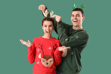 Sticker - Young couple in Christmas sweaters and reindeer horns on green background