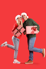 Wall Mural - Young couple in Santa hats with Christmas gifts on red background