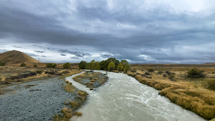 Wall Mural - Flooded stream on the winding narrow gravel road between Lake Tekapo and Lake Pukaki in rural agricultural land