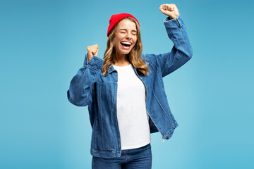 Wall Mural - Portrait of positive young woman wearing red hat and stylish denim shirt, with closed eyes dancing