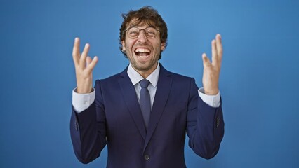 Wall Mural - Excited young man in business suit goes wild, celebrating win with arms aloft. bubbles over with joy on isolated blue background. victory has never looked this handsome.
