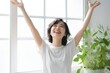 Joyful woman raising arms in front of window with natural light pouring in, feeling free and alive Generative AI