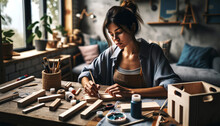 A 28-year-old Woman Focused On A DIY Project In A Well-lit Home Workspace. DIY Materials Like Wood, Tools, And Paints Are Neatly Arranged On The Table