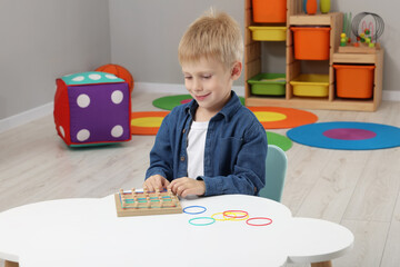 Wall Mural - Motor skills development. Boy playing with geoboard and rubber bands at white table in room