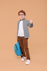 Sticker - Happy schoolboy with backpack showing thumb up on beige background