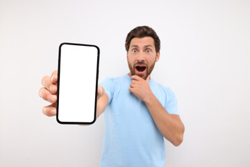 Poster - Surprised man showing smartphone in hand on white background, selective focus. Mockup for design