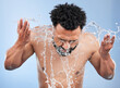 Black man, water splash and face wash for skincare, hygiene or grooming against a blue studio background. African male person, model and aqua for body hydration, shower or facial skin treatment