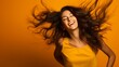 © Suleyman - Bright young lady in a studio twisting her hair in a playful way; joyful woman dancing and rejoicing against an orange backdrop