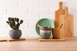 Set of ceramic bowls and cutting boards on wooden light countertop in modern kitchen with potted opuntia, cactus. Front view. minimalism.