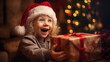 A child with curly hair and a Christmas hat is happily receiving the present and is amused and smiling