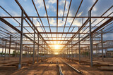 Fototapeta Miasto - The structure of steel framing at construction site against a vast cloudy sky with bright sun behind. New build home at empty lot. framework ready for wall and roof install. Real estate development